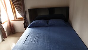 Una cama individual con colchón y almohadas azul oscuro, una ventana con cortinas y una pared lisa.