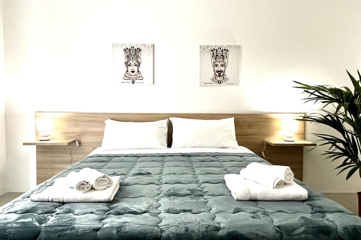 A hotel room with a bed, two bedside tables, a nightstand, and a potted plant.