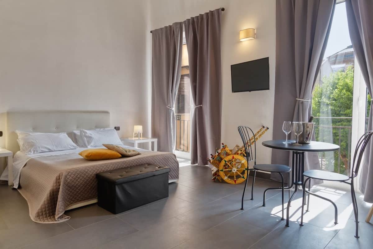 A modern hotel room with a bed, bedside tables, a small table with glasses, and a chair.