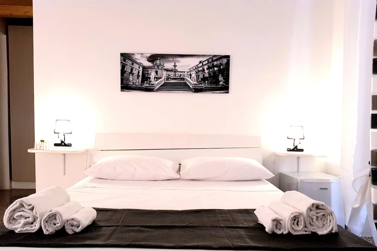 A neatly made bed with white linens, two bedside tables with lamps, and a black and white photograph on the wall.