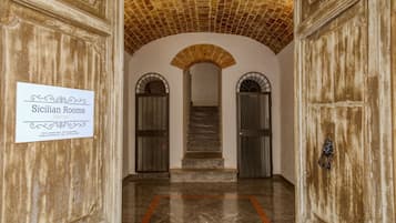 Un corridoio con una targa che indica le Stanze Siciliane a Palermo, con soffitto in mattoni, porte ad arco e pavimento in marmo.
