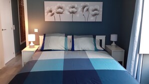 Une chambre à coucher comprenant un lit, deux tables de chevet, une œuvre d’art accrochée au mur et une fenêtre avec des rideaux.