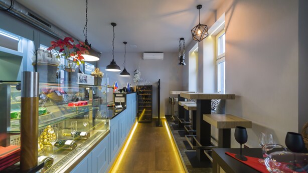 Zona de bar moderna con una vitrina de vidrio, lámparas colgantes y un banco de madera.