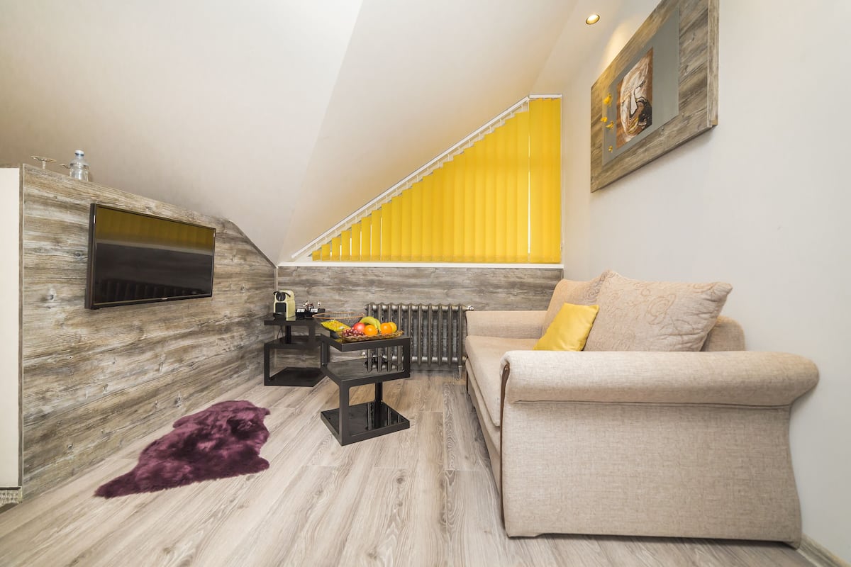 Una sala de estar moderna con un sofá, una mesa de centro con fruta, un televisor y una escalera con barandillas amarillas.