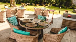 Un patio al aire libre con mobiliario de mimbre, incluyendo mesas y sillas redondas, dispuesto para comer.