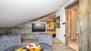 Una sala de estar moderna con un televisor de pantalla plana, dos sofás grises y una cesta de frutas sobre una mesa auxiliar.