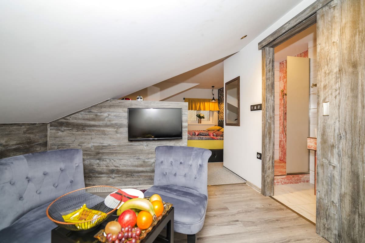 Una sala de estar moderna con un televisor de pantalla plana, dos sofás grises y una cesta de frutas sobre una mesa auxiliar.