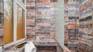Un baño de diseño rústico, con ducha de mampara de vidrio, toallero y ventana con persianas.