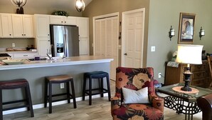 A modern kitchen with a central island, bar stools, and a floral armchair.