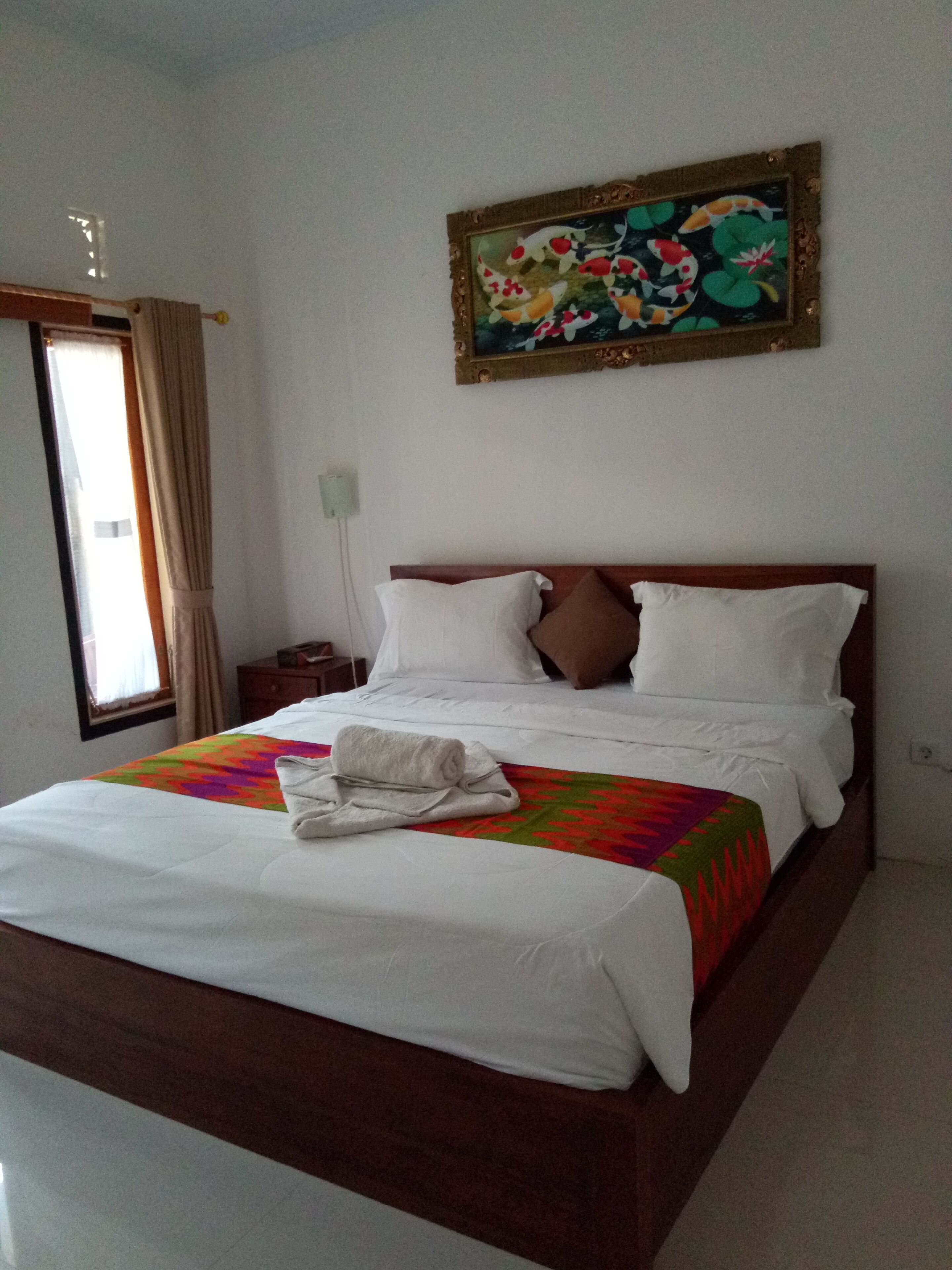 Una habitación de hotel con una cama, un cuadro en la pared y una ventana con cortinas.