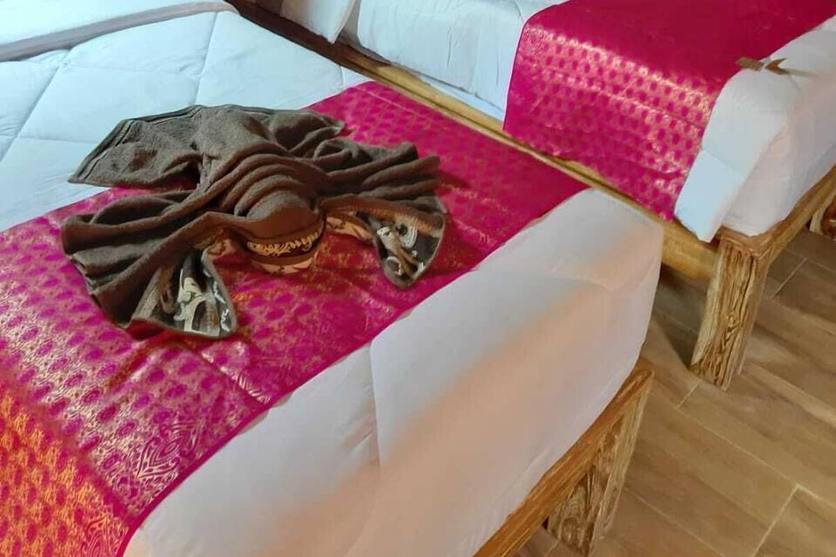 Une pièce avec deux lits en bois, chacun étant muni d’un matelas blanc et d’une couverture rose. Le lit de gauche a une tête de lit en bois, tout comme le lit de droite.