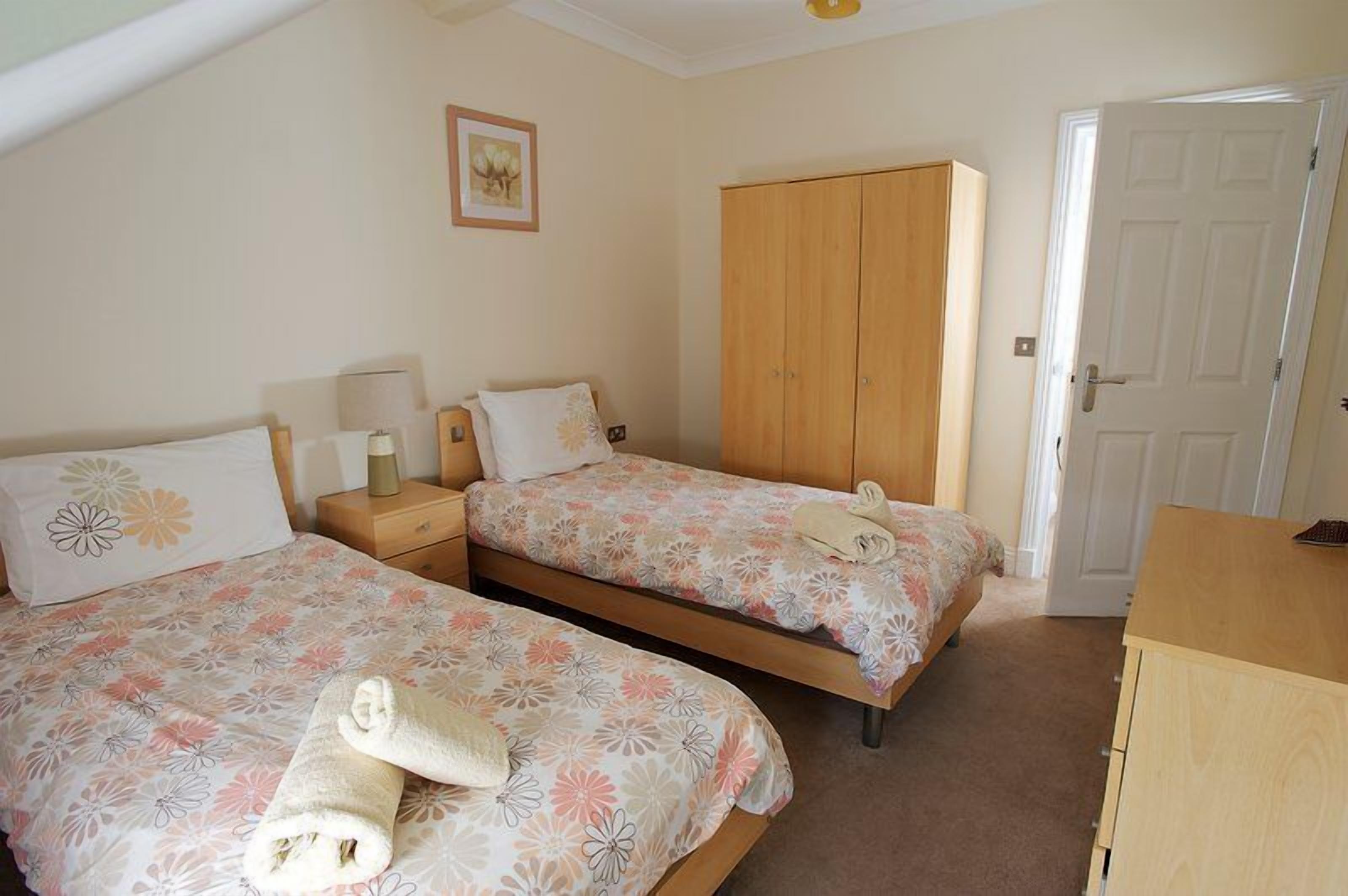 A bedroom with two beds, a wardrobe, a desk, and a door.