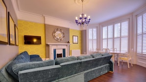 A living room with a sectional sofa, a fireplace, a chandelier, and a dining area with a table and chairs. - Opulence (Bournemouth)