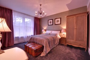 Ein Schlafzimmer mit einem großen Bett, einem Holzschrank, einer Kommode, einem Nachttisch, einer Lampe und einem Fenster mit Vorhängen.