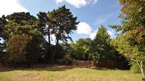 A backyard with a large tree, a wooden fence, and a grassy lawn. - Opulence (Bournemouth)