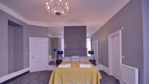 A bedroom with a large bed, a chandelier, and a mirror on the wall. - Opulence (Bournemouth)
