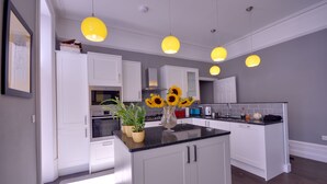 A modern kitchen with white cabinets, a central island, and yellow pendant lights. - Opulence (Bournemouth)