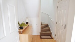 Un couloir avec un escalier menant à l’étage supérieur, une petite table avec une plante et une porte.