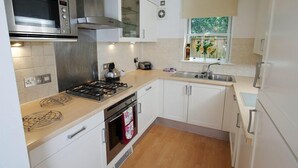 Une cuisine moderne avec des meubles blancs, un four à micro-ondes en acier inoxydable, une cuisinière à gaz et un four encastré.
