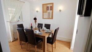 Un coin repas avec une table en bois, des chaises noires et un mur blanc orné d’un tableau encadré.
