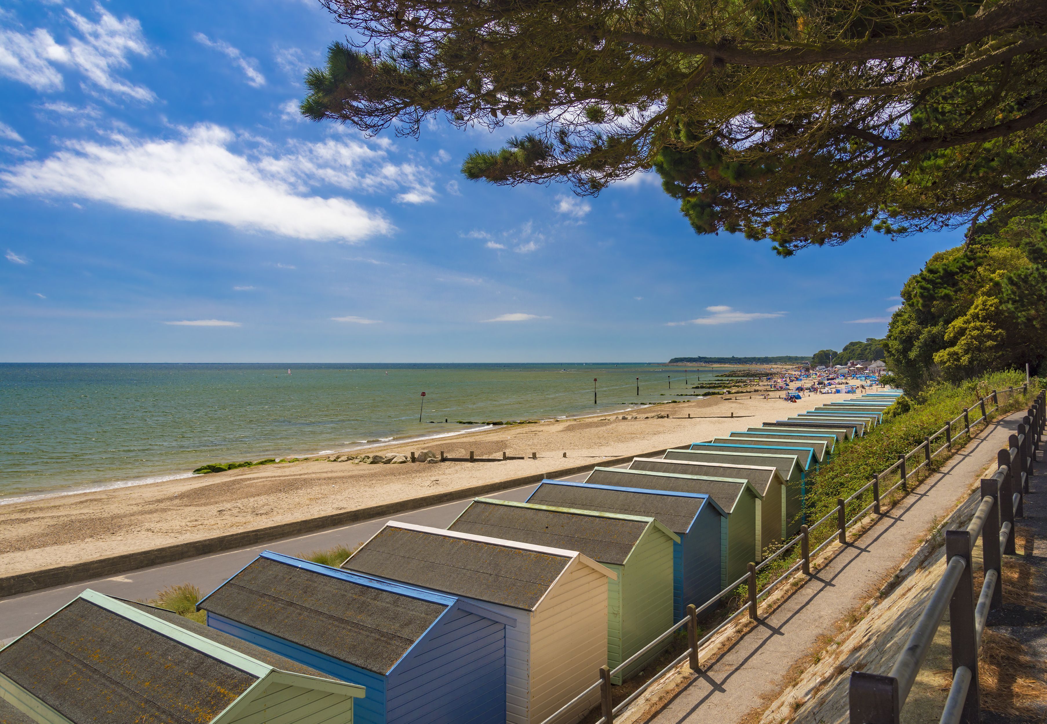 A row of beachside beach huts with a view of the sea and beach.