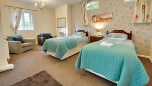 A bedroom with two beds, a sofa, a small table, and a window with curtains. - Somerville Coach House 2 (Bournemouth)