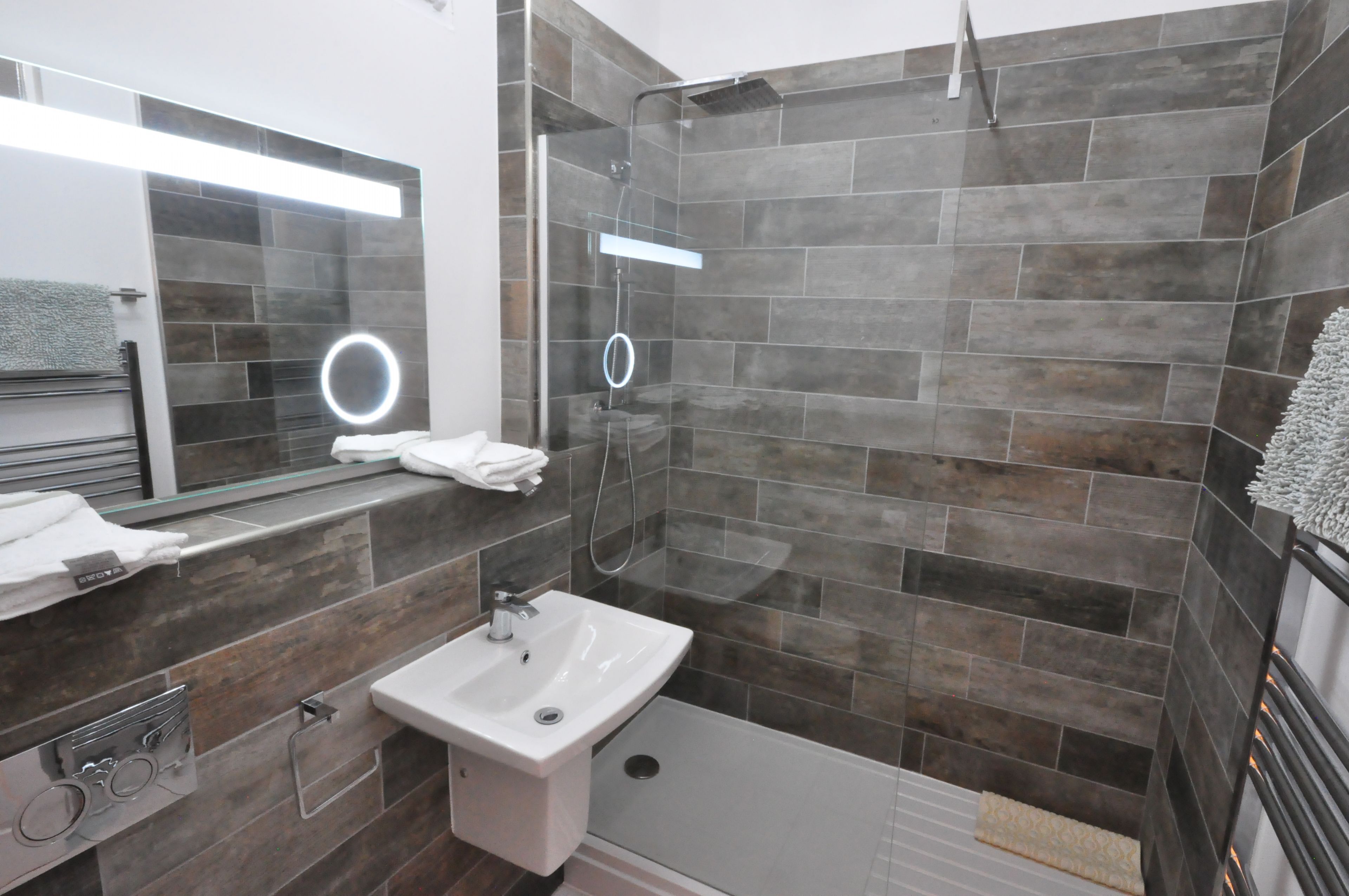 A modern bathroom with a glass-enclosed shower, a white sink, and a large mirror with a circular light.