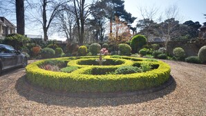 Un jardí circular amb taronja tallada i una font central, envoltat de grava i arbres.