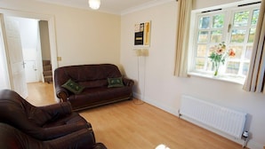 A living room with a brown leather sofa, a standing floor lamp, a radiator, and a window with curtains. - Shell Cottage (Bournemouth)