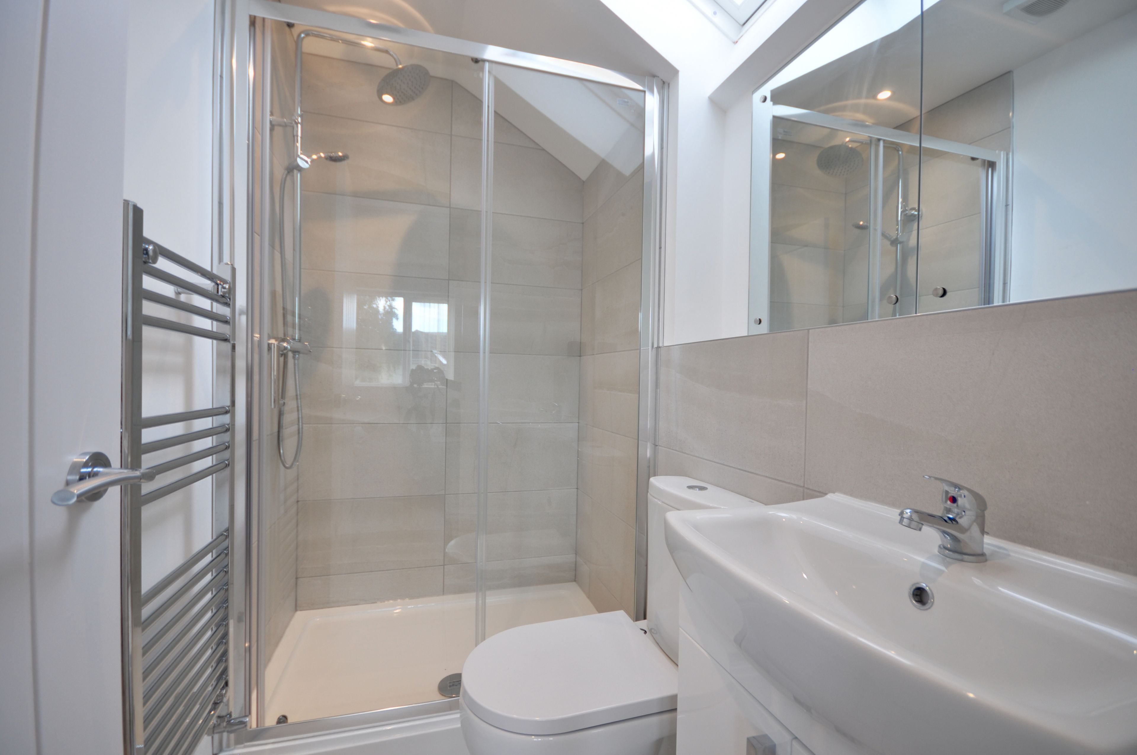 Un baño moderno con ducha de mampara de vidrio, inodoro blanco y un lavamanos grande con espejo arriba.