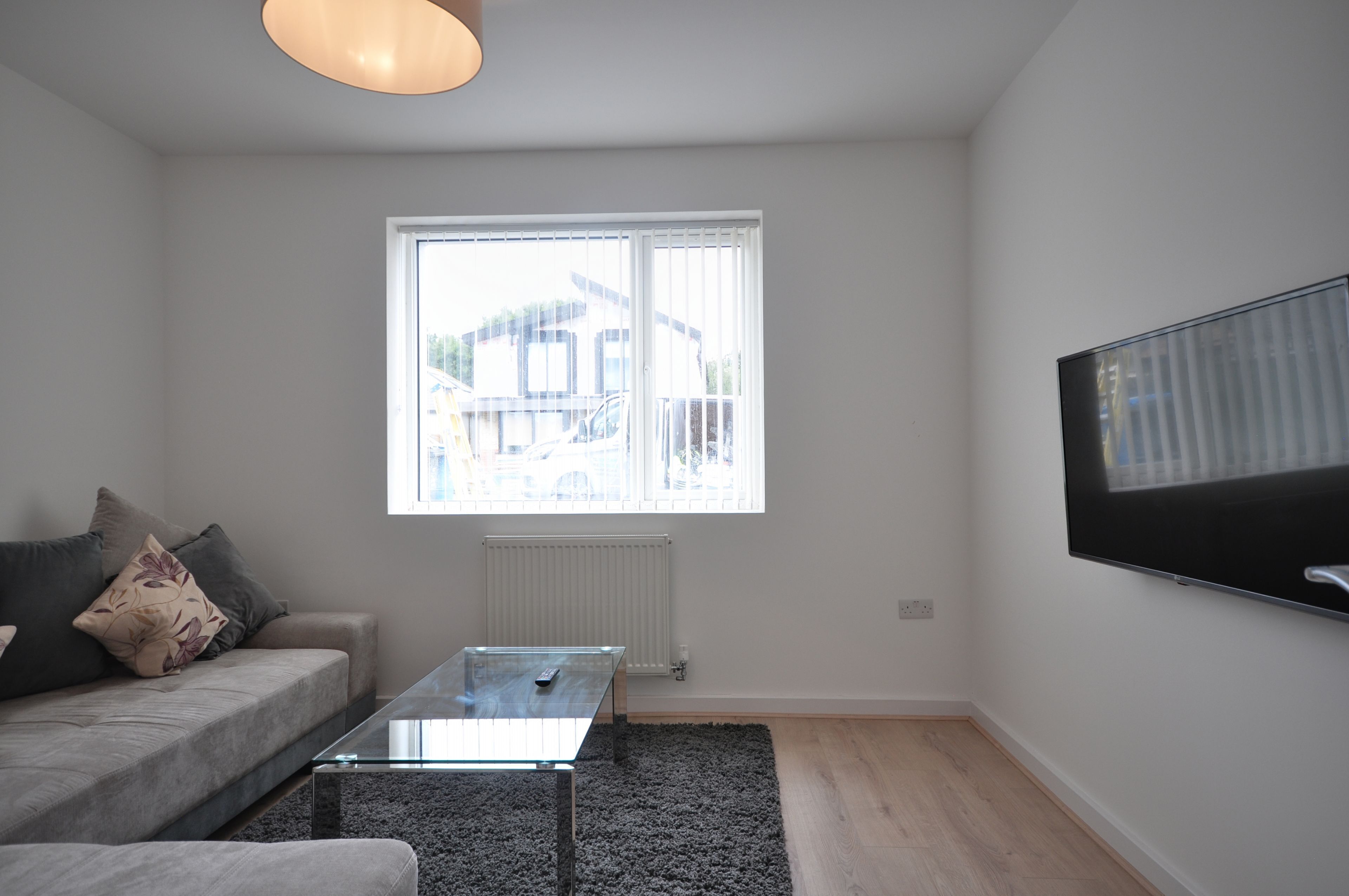 Un salon moderne avec un canapé, une table basse en verre, une grande fenêtre et un téléviseur fixé au mur.