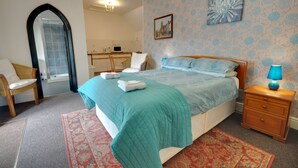 A bedroom with a bed, a nightstand, a chair, a mirror, a bathroom, and a patterned wall. - Somerville Coach House 4 (Bournemouth)