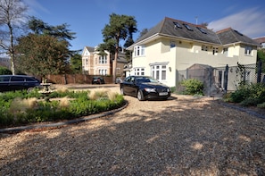A residential driveway with a gravel surface, a black car parked, and a house with a sloped roof and multiple windows. - Somerville Coach House 4 (Bournemouth)
