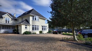 A two-story house with a gravel driveway and a tree in the foreground. - Somerville Coach House 4 (Bournemouth)
