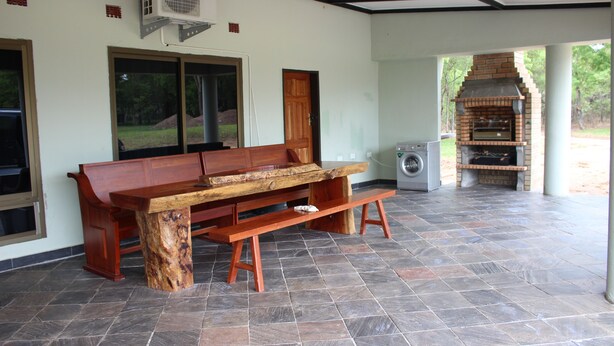A covered patio area with a wooden bench, a brick oven, and a washing machine. - Waterfalls Apartments (Lusaka)