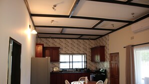A kitchen with a dining area, wooden cabinets, a refrigerator, and a window with blinds. - Waterfalls Apartments (Lusaka)