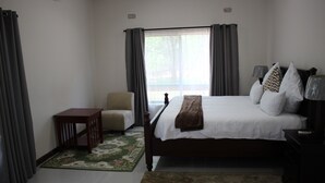 A bedroom with a bed, a chair, a nightstand, and a window with curtains. - Waterfalls Apartments (Lusaka)