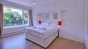 A modern bedroom with a large bed, built-in storage cabinets, and a window with a view of greenery. - The Breaking Surf (Poole)