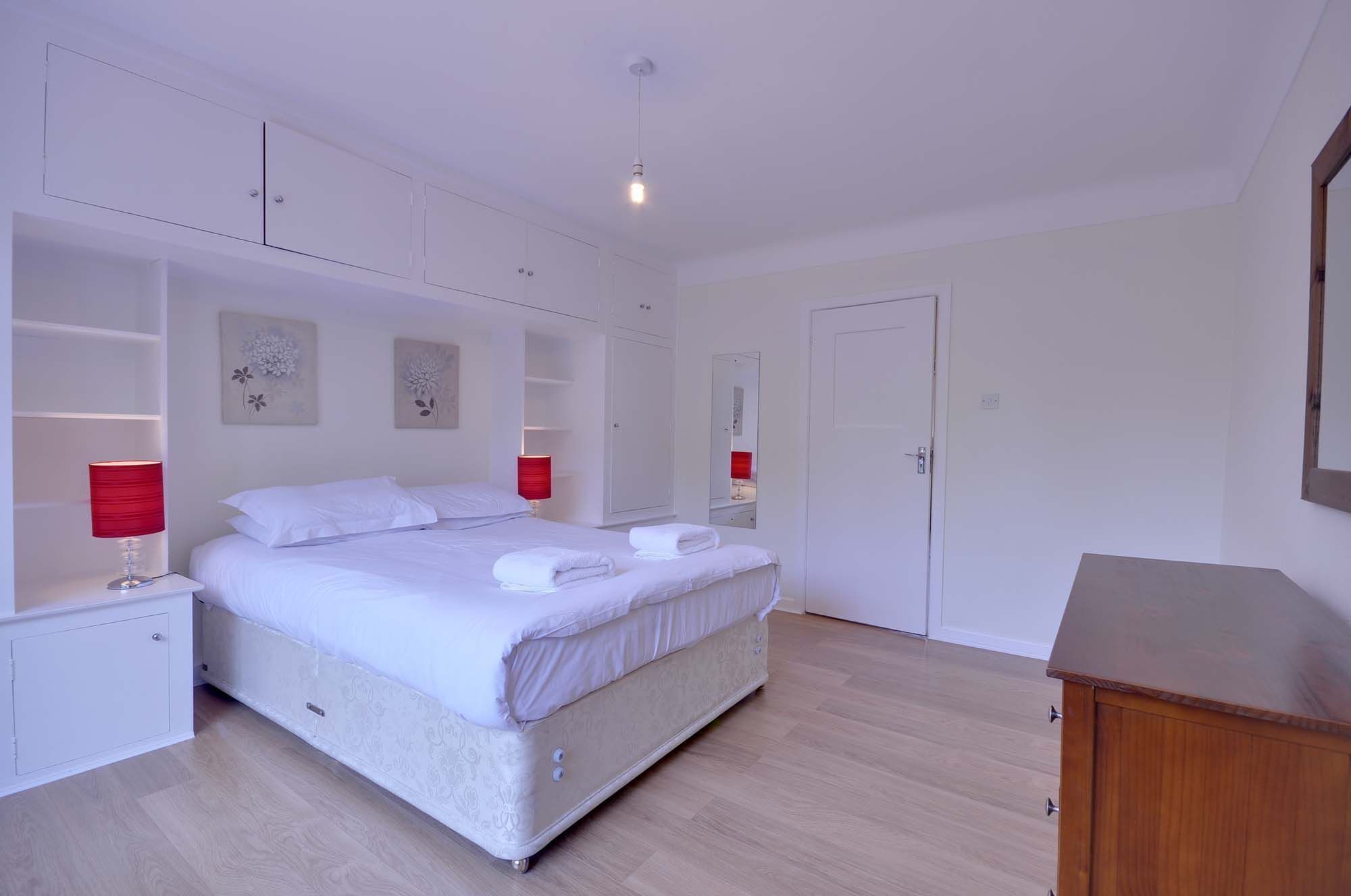 A bedroom with a large bed, two bedside tables with lamps, a wardrobe, and a mirror.