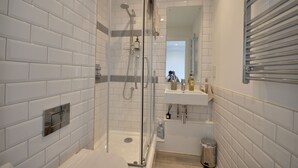 Un baño moderno con azulejos blancos tipo metro, ducha con cerramiento de vidrio, lavabo blanco con espejo y barra para toallas.