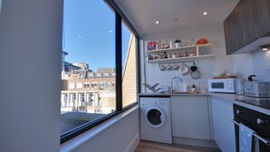 Cocina compacta con lavadora, microondas y horno. Un ventanal grande ofrece vistas de la ciudad.