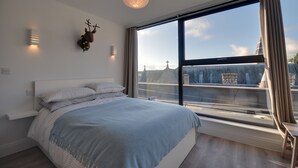 Un dormitorio moderno con un ventanal grande, una cama con manta azul y una decoración de reno en la pared.