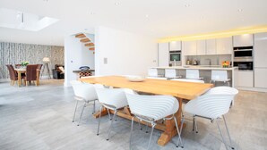 A modern kitchen with white cabinets, a wooden dining table, and white chairs. - Spyglass (Poole)