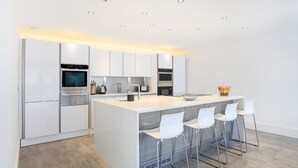 A modern kitchen with white cabinetry, stainless steel appliances, and a central island with bar stools. - Spyglass (Poole)