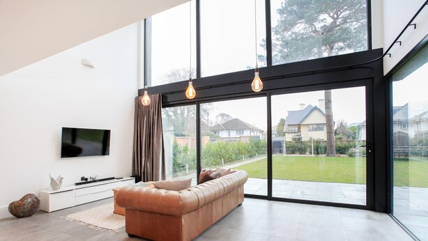 A modern living room with a large window, a leather sofa, a flat-screen TV, and a minimalist console table. - Spyglass (Poole)
