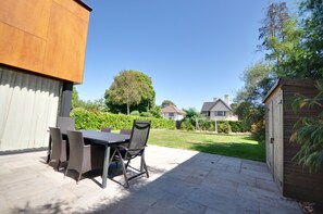 Un patio al aire libre con una mesa y sillas, un cobertizo de madera y un césped bien cuidado.