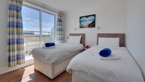 Habitación de hotel con dos camas, un ventanal con cortinas y una imagen con forma de corazón en la pared, con vista al mar.