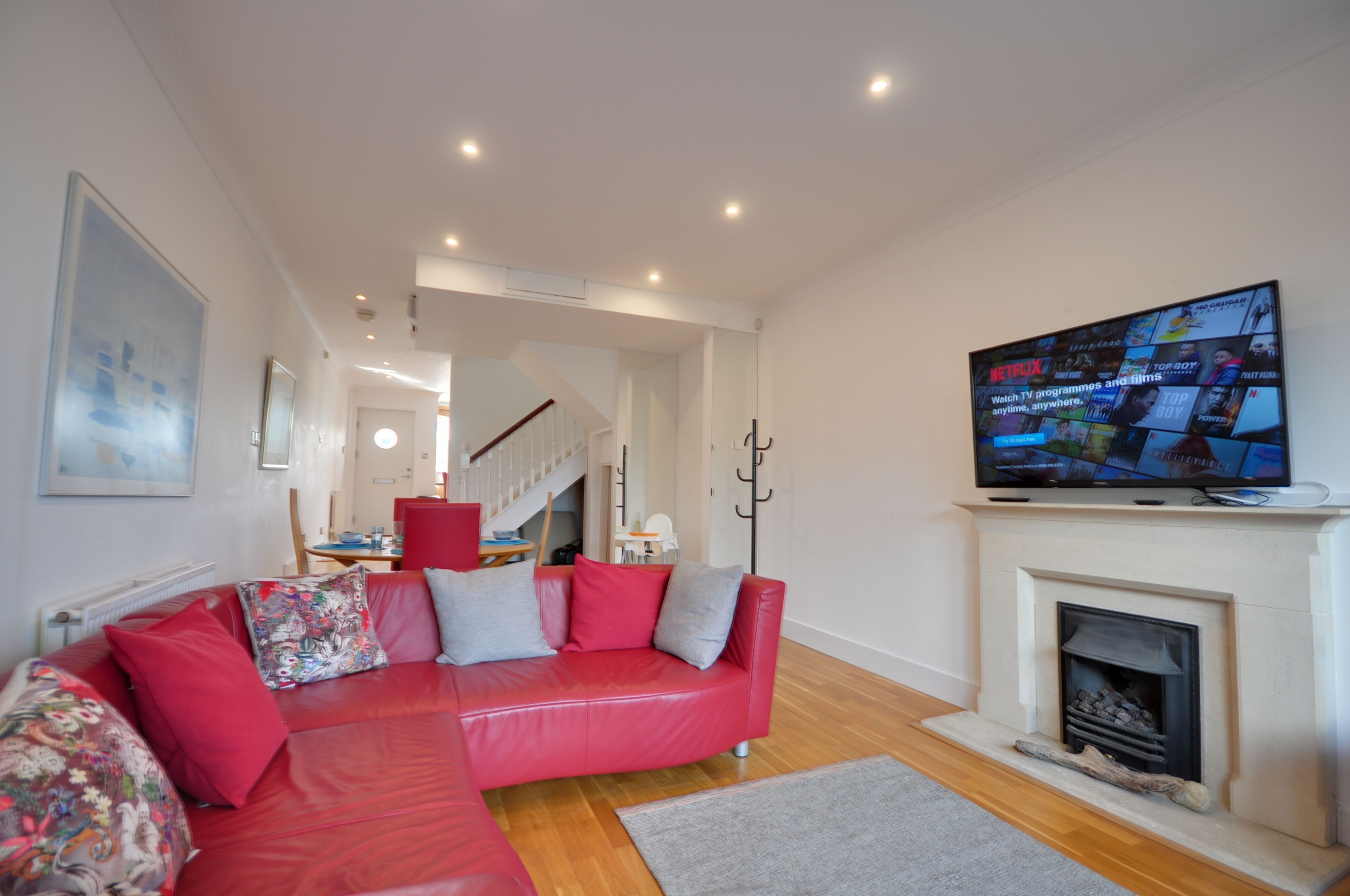 Una sala moderna con un sofá rojo, una chimenea y un televisor montado que muestra contenido de Netflix.