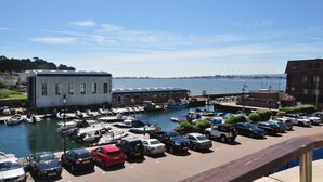 Un puerto deportivo con barcos amarrados, una zona de aparcamiento con coches y un edificio con techo plano.