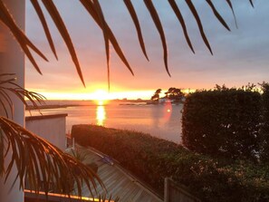 Vista al tramonto da un balcone su un corpo d'acqua, con un pontile in legno e vegetazione sullo sfondo.